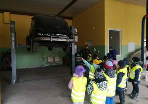Tata Oliwci, prezentuje dzieciom w jaki sposób działa podnośnik samochodowy